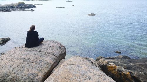 Rear view of woman sitting on rock looking at sea