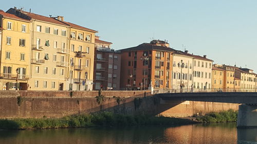 Bridge over river by buildings against clear sky