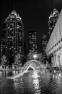 Illuminated bridge over river by buildings in city at night