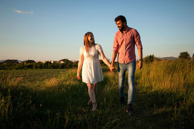 Young couple standing on field against sky