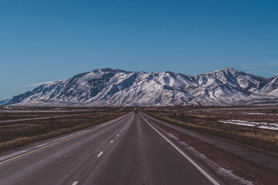 Road leading towards mountain against clear blue sky