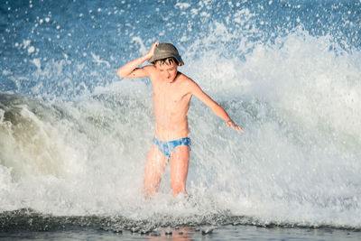 Full length of shirtless man splashing water in sea