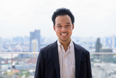 Portrait of smiling young man standing against cityscape