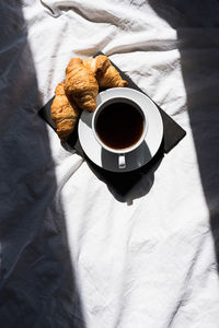 Coffee cup and croissants on the bed in morning sunlight. trendy still life with interesting shadow.
