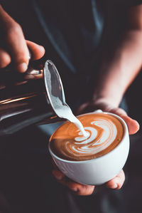 Midsection of barista pouring milk in coffee at cafe