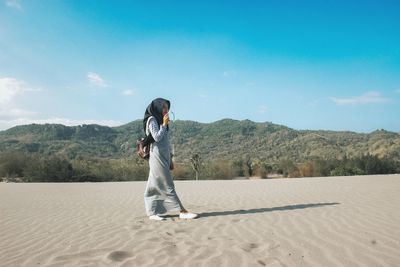 Side view of woman standing on sand against sky