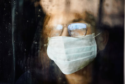 Woman looking through the wet window during stay home while covid-19