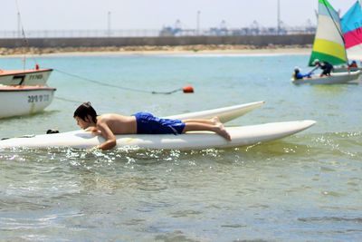 Full length of shirtless boy surfboarding in sea