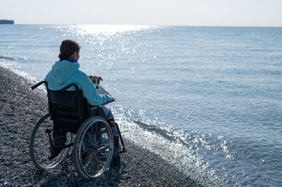 Rear view of man sitting on sea against sky