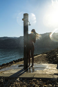 Woman taking shower while standing against clear sky during sunset