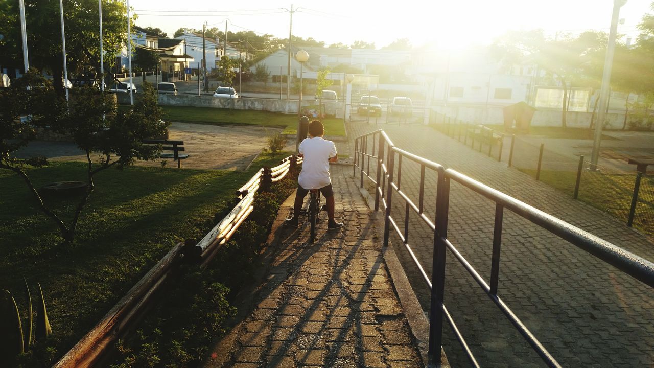 full length, lifestyles, the way forward, rear view, railroad track, walking, railing, sunlight, leisure activity, built structure, casual clothing, transportation, diminishing perspective, building exterior, men, architecture, vanishing point, standing