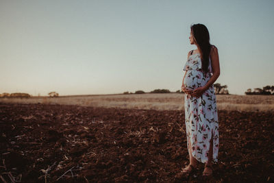 Pregnant woman standing on field against clear sky during sunset