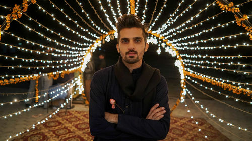 Portrait of young man standing against illuminated lights at night