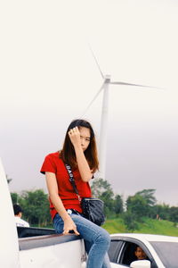 Portrait of woman sitting by windmill against sky