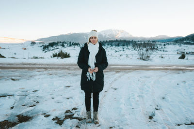 Woman in hat and scarf outdoors in snow with mountain peak in the background