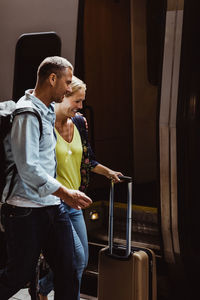 Happy couple with luggage walking by train at railroad station
