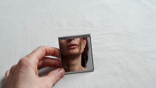 Cropped hand of woman holding mirror over table