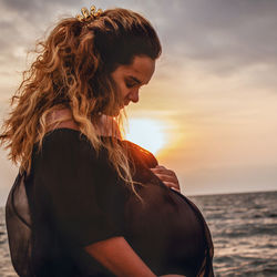 Pregnant woman on beach against sky during sunset