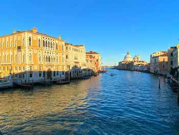 Buildings by river against clear blue sky