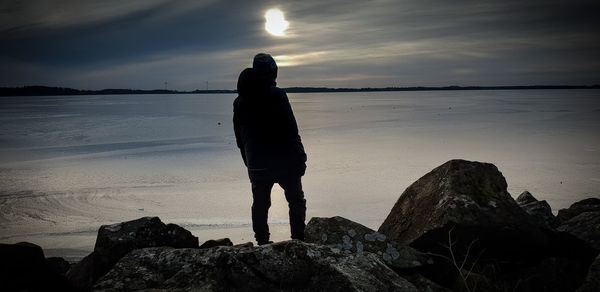 Man standing on rock at beach against sky during sunset