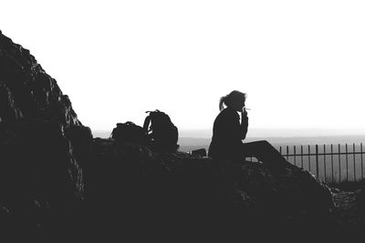 Silhouette of man photographing dog against clear sky