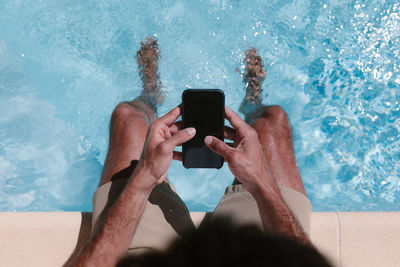 Midsection of man using mobile phone in swimming pool