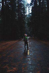 Full length of man showing middle finger while standing on road at forest