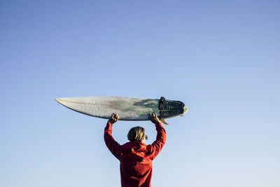 Rear view of man holding umbrella against clear blue sky