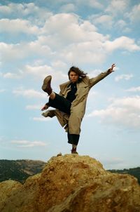 Full length of woman standing on rock against sky