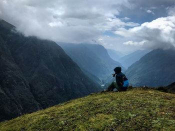 Side view of woman sitting on mountain against cloudy sky