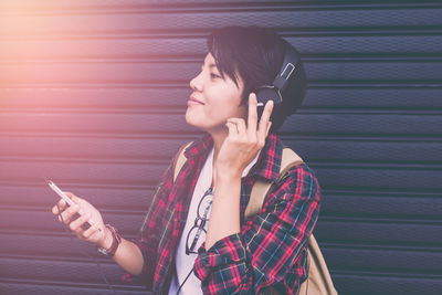 Young woman using mobile phone against wall