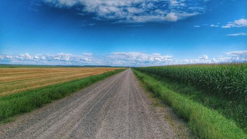 Road passing through field against cloudy sky