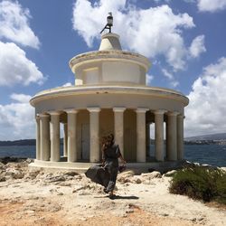 Full length of man sitting on stone wall against sky