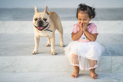 Full length of cute girl laughing while sitting by dog on staircase