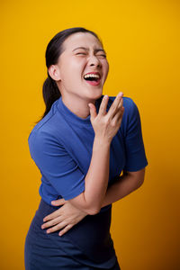 Young woman looking away while standing against yellow background