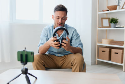 Young man sitting on chair with wireless headphones at home