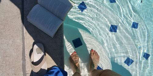 Low section of woman standing in swimming pool by book and flip-flop