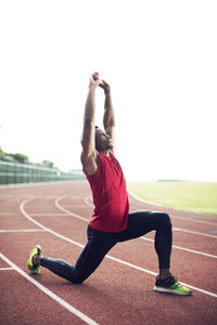 Full length of male athlete exercising on running tracks against clear sky