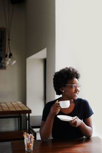 Young woman holding coffee while sitting on table