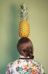 Close-up of woman holding pineapple against green background