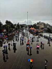 People on wet street in city against sky