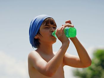 Portrait of shirtless boy holding ice cream against sky