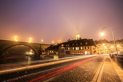 Illuminated railroad tracks in city against sky at night bern