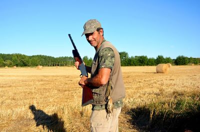 Portrait of man holding gun while standing on field