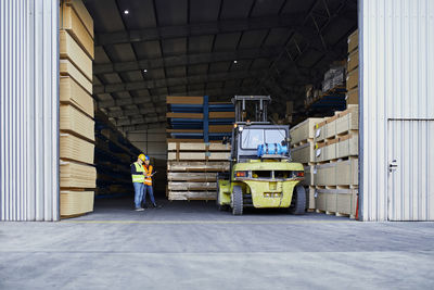 Two workers standing in factory warehouse next to forklift