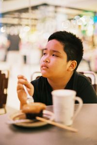 Boy by coffee cup on table at restaurant