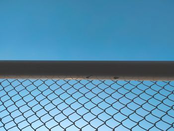 Low angle view of chainlink fence against clear blue sky