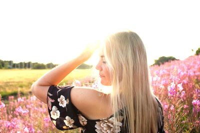Rear view of young woman standing on flowering field during sunny day