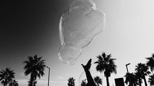 Cropped hand reaching to bubbles against clear sky
