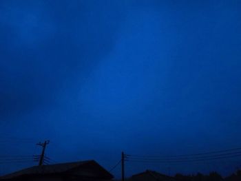 Low angle view of silhouette communications tower against blue sky